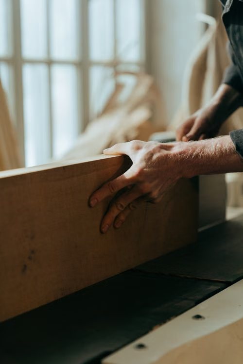 Hands guiding a solid wood board along a workshop machine