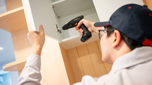 Installer drilling a hinge on a wall cabinet door with a cordless drill