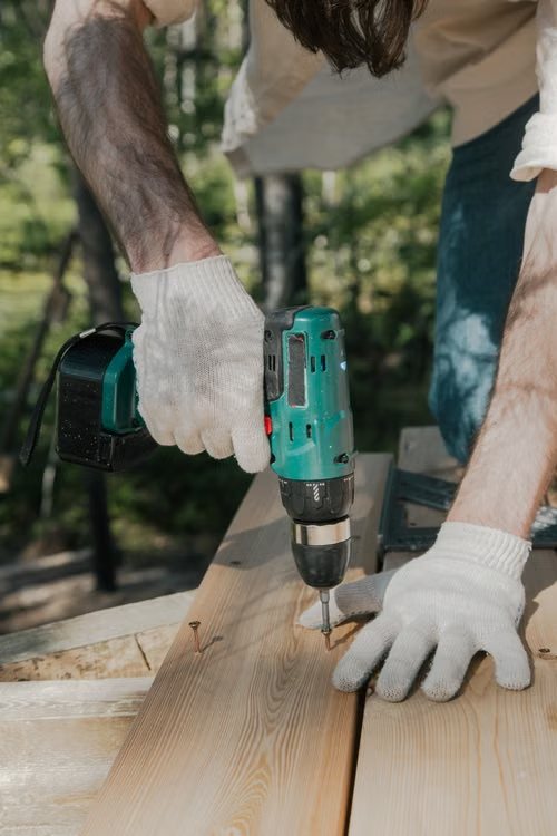 Worker in gloves driving a screw into deck boards with a cordless drill