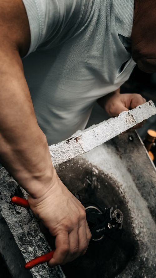 Hands using red-handled pliers on a stone basin